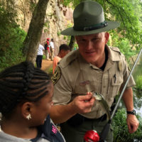 A Virginia State Park Ranger holding a fish for a park visitor.