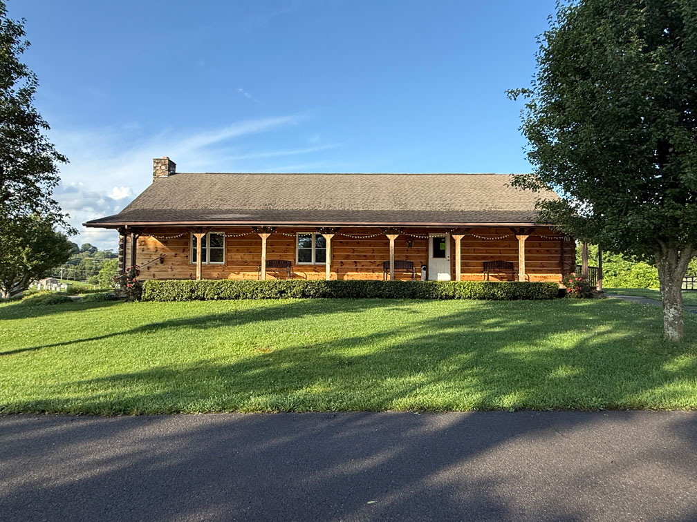 Front view of Keith Memorial Park event cabin with manicured lawn, trees, and string lights on the porch.